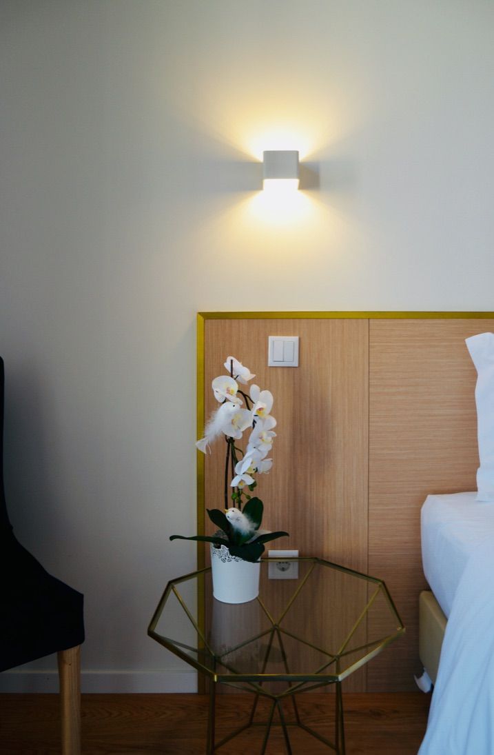 A hotel room with a wooden headboard, a glass table with a white orchid, and a wall-mounted light fixture.