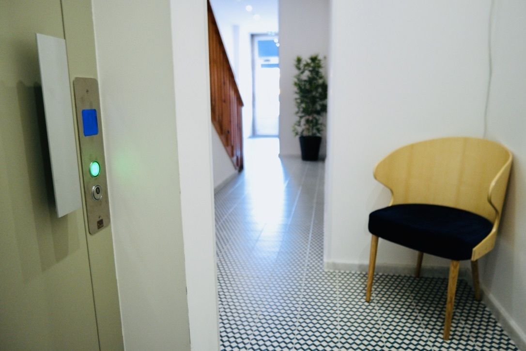 A hallway with a patterned floor, a chair, and a door with a control panel.