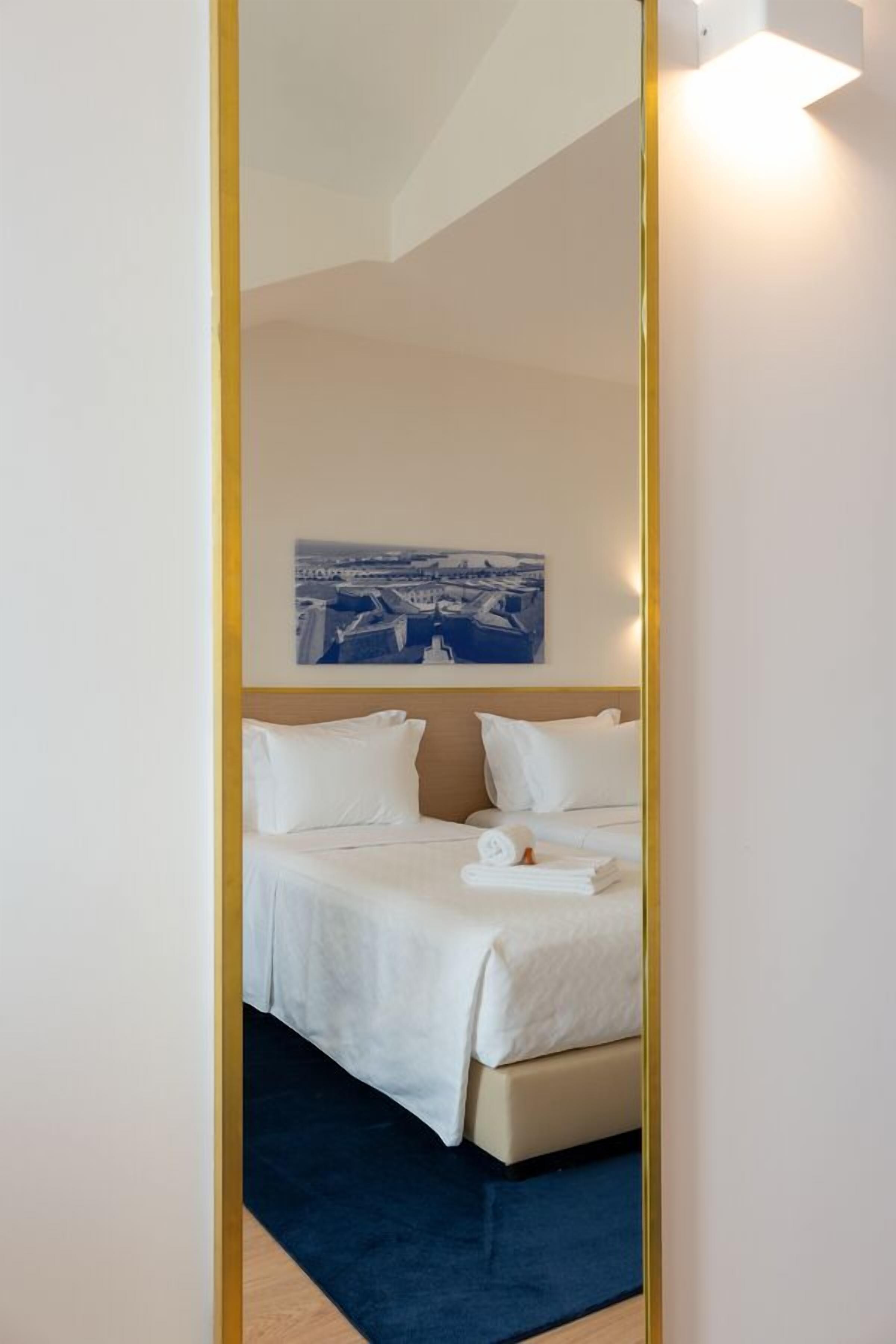 A hotel room with a bed, a blue rug, and a cityscape painting on the wall.