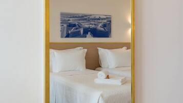 A hotel room with a bed, a blue rug, and a cityscape painting on the wall.
