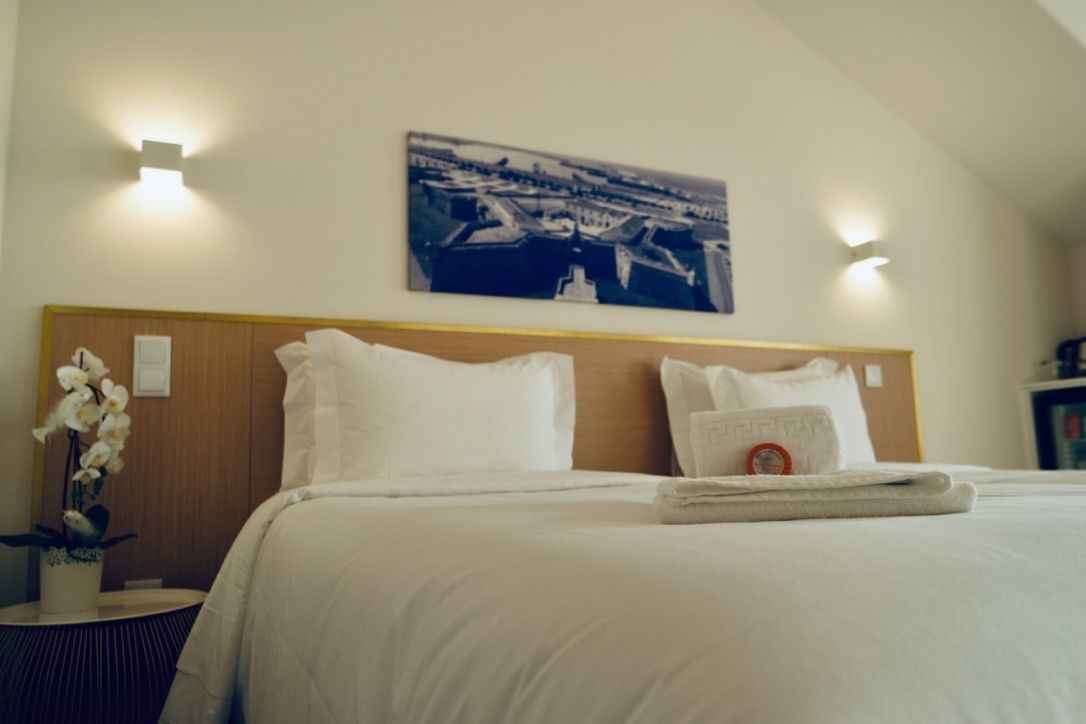 A hotel room with a neatly made bed, a headboard, a wall-mounted painting, and a small table with a plant.