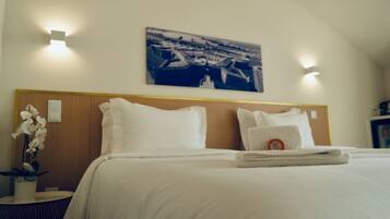 A hotel room with a neatly made bed, a headboard, a wall-mounted painting, and a small table with a plant.