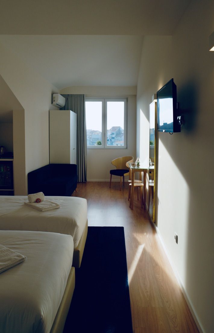 A hotel room with two beds, a desk, a chair, a TV, and a window with a city view.