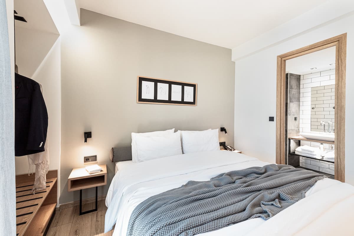 Une chambre d’hôtel moderne avec un grand lit, une table de chevet, un miroir et un tableau encadré au mur.