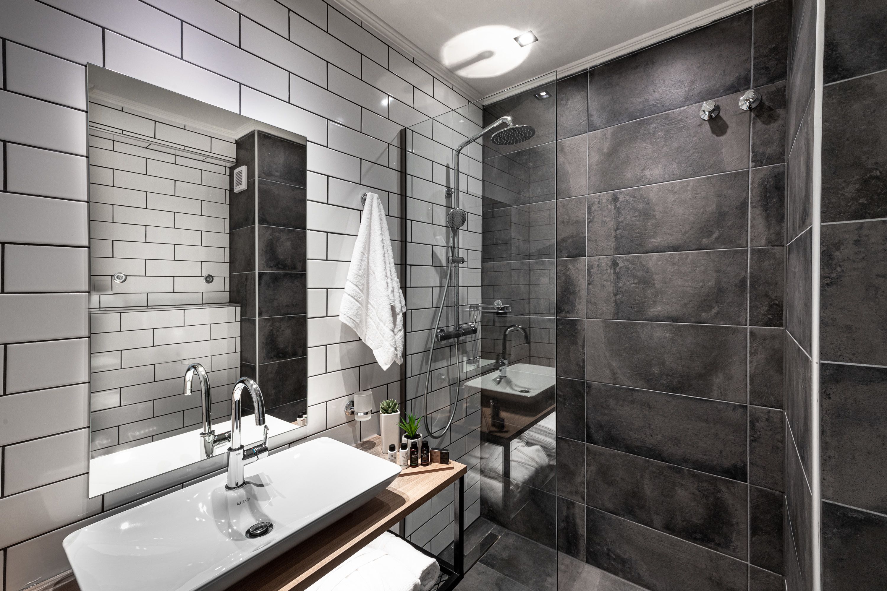 Un baño moderno con un espejo grande, un lavabo, una ducha y una toalla colgada en la pared.
