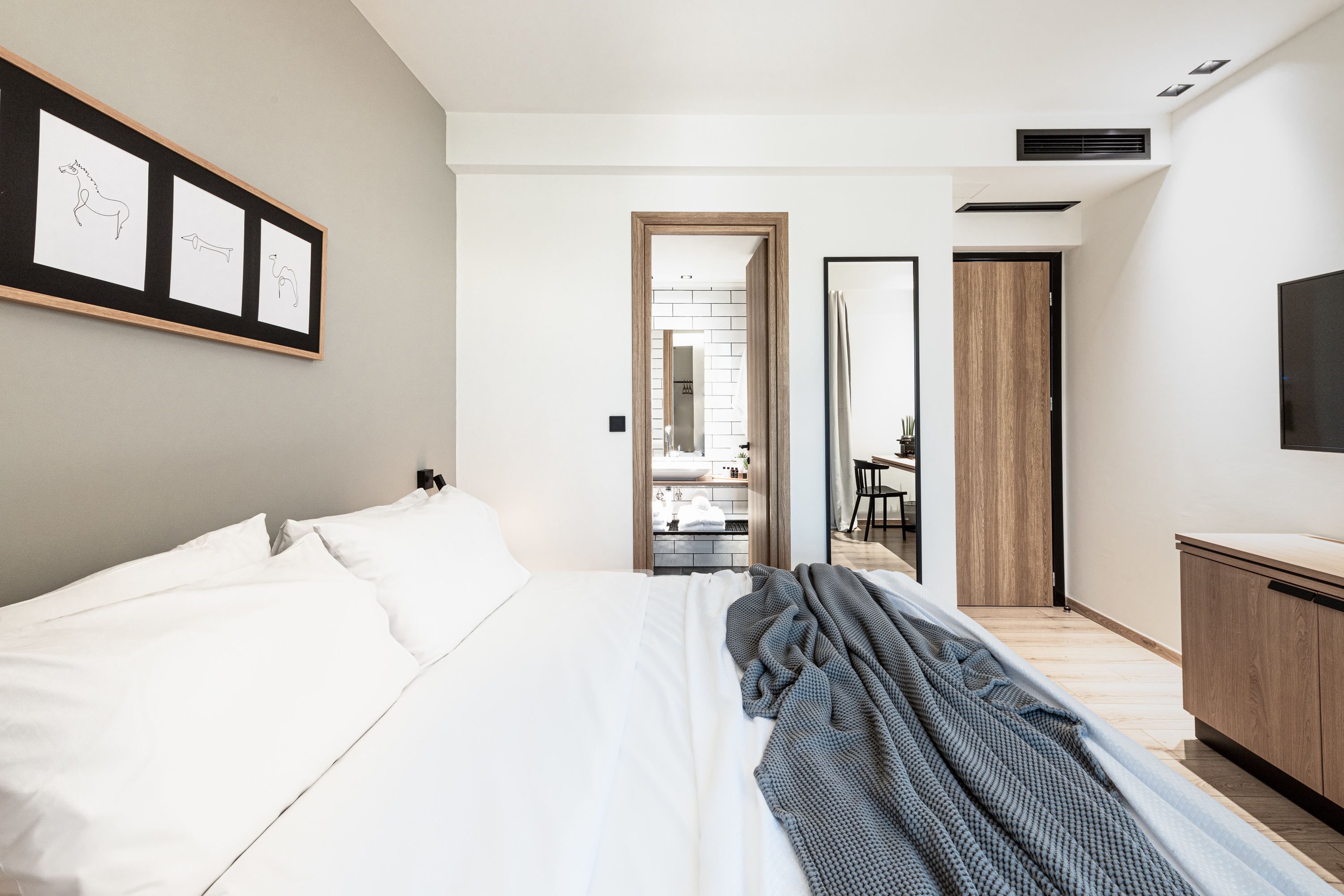 A modern hotel room with a large bed, a TV, a wooden wardrobe, and a framed picture on the wall.
