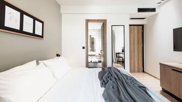 A modern hotel room with a large bed, a TV, a wooden wardrobe, and a framed picture on the wall.