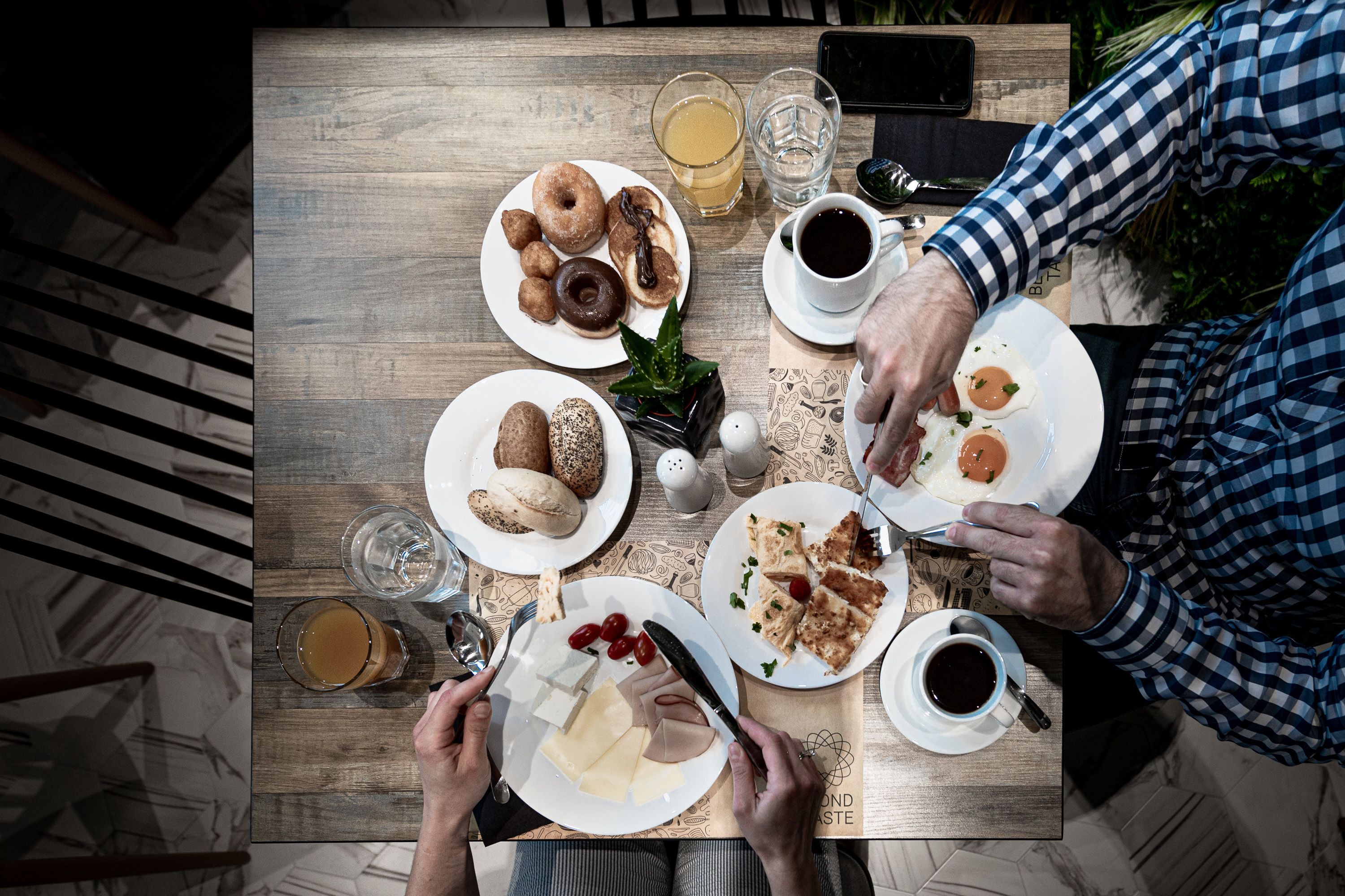 Uma mesa de madeira com pratos de comida, copos de bebidas e um smartphone.