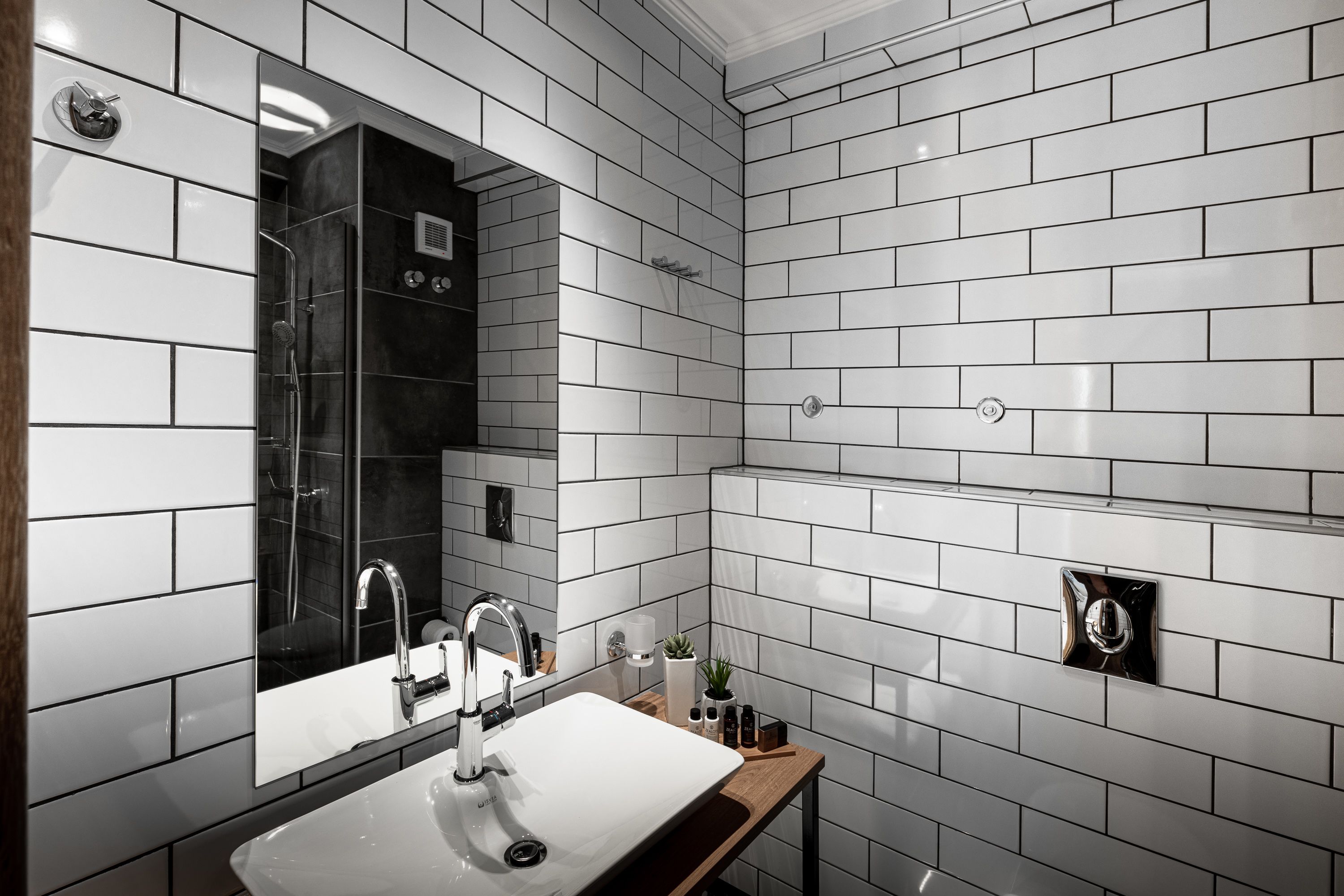A modern bathroom with white subway tiles, a large mirror, a sink with a faucet, and a shower area.