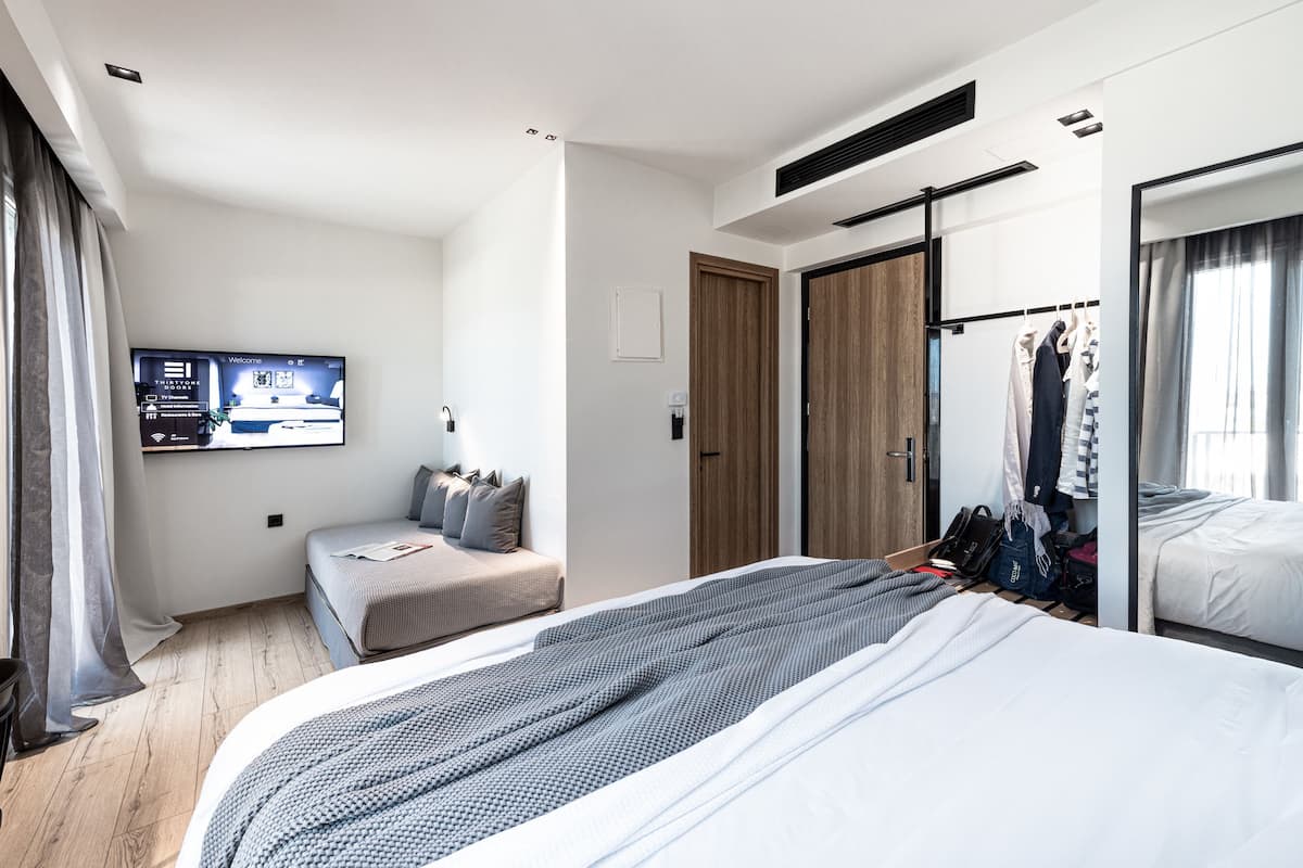 Une chambre d’hôtel moderne dotée d’un grand lit, d’un petit canapé, d’un téléviseur fixé au mur et d’une armoire avec un miroir.