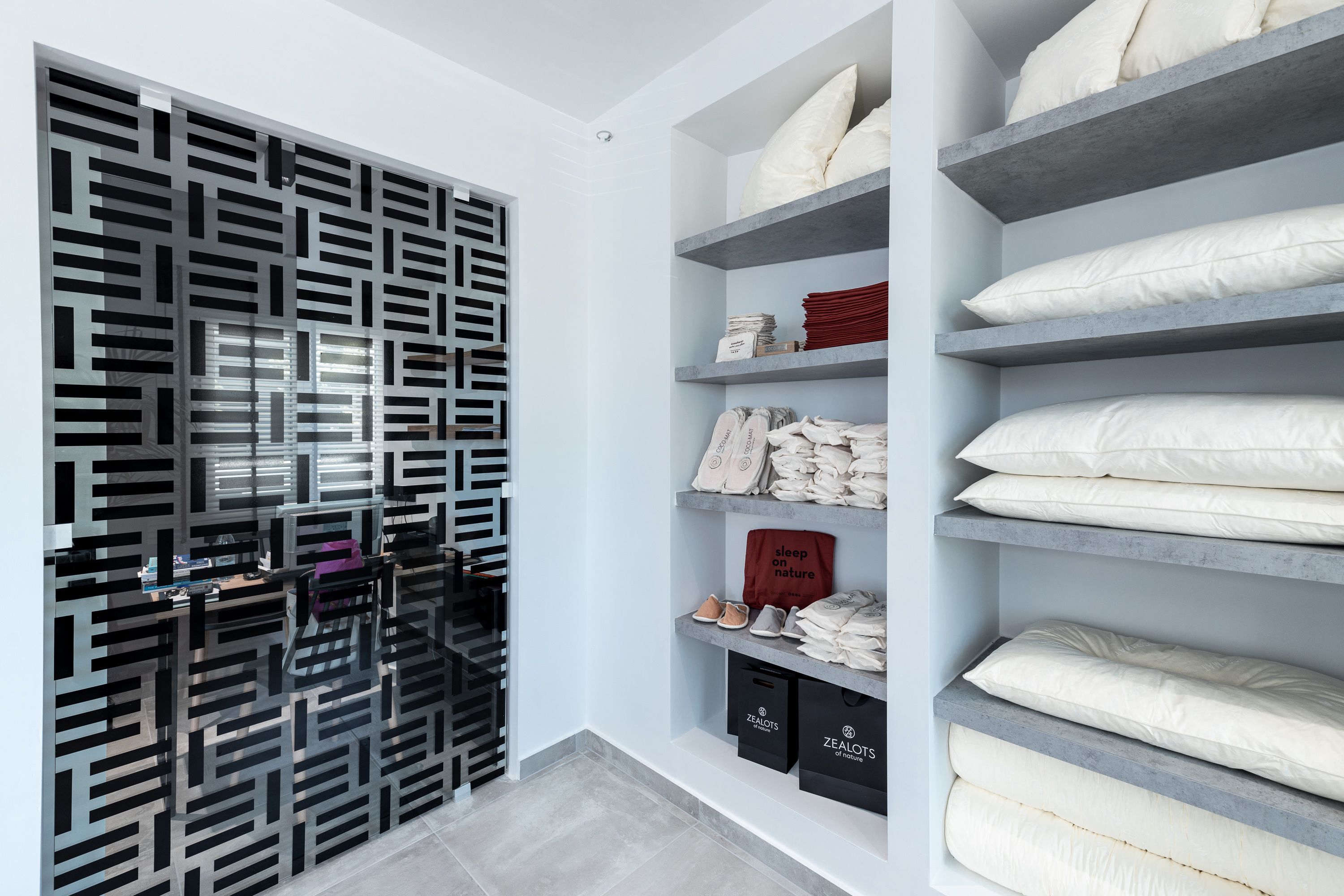 Quarto moderno com parede estampada em padrão geométrico, nichos com roupa de cama dobrada e um sapateiro.