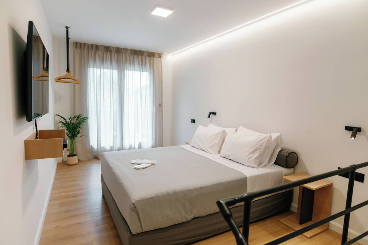 Une chambre à coucher moderne avec un lit, un téléviseur fixé au mur, une plante en pot et une fenêtre avec des rideaux.