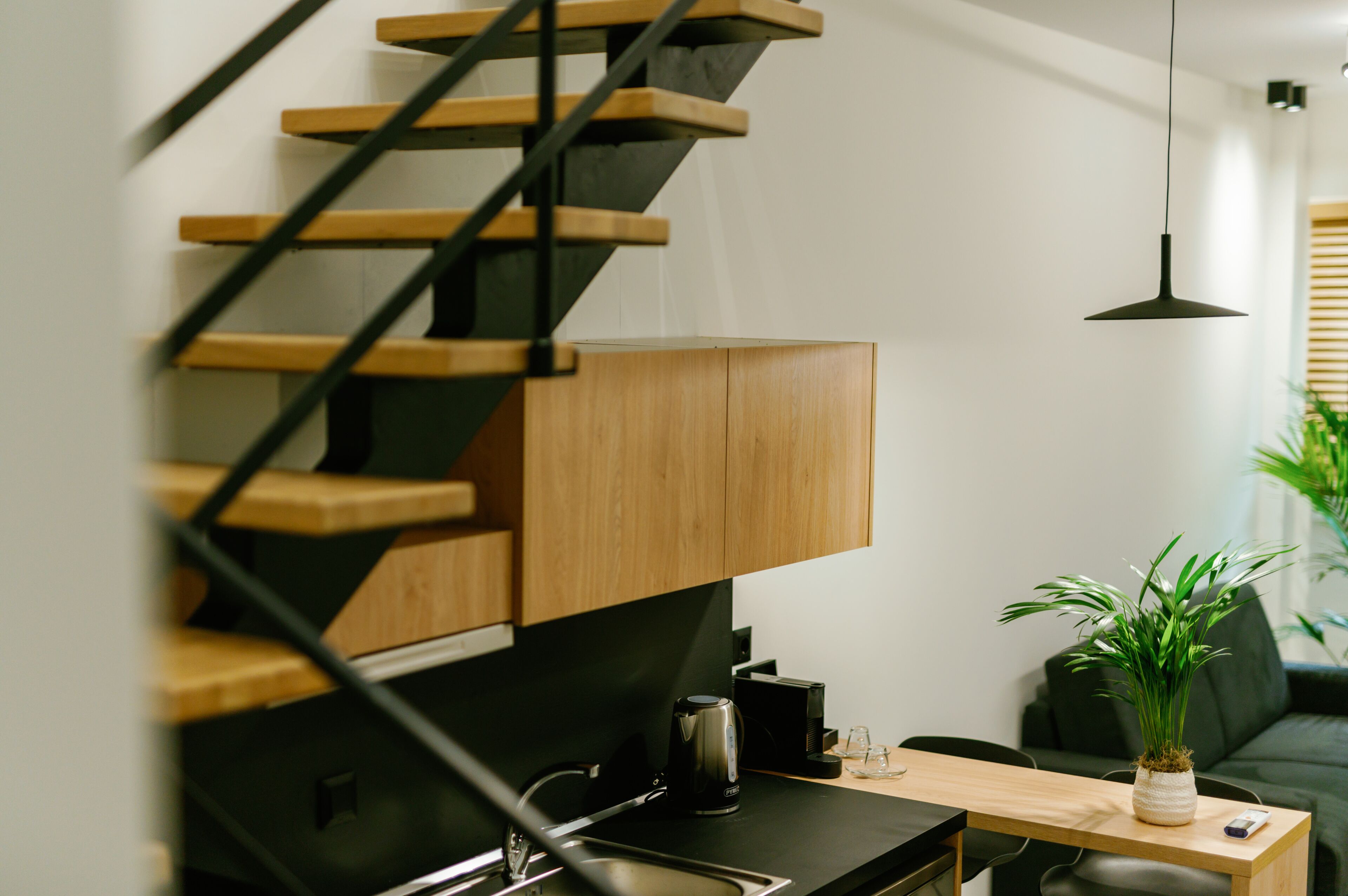 Una cocina moderna con escalera de madera, una cafetera y una planta en maceta.
