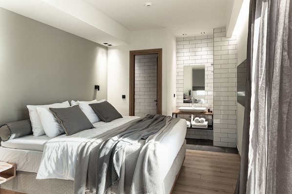 Un dormitorio moderno con una cama grande, una mesita de noche, un espejo y un baño con lavamanos y perchero para toallas.