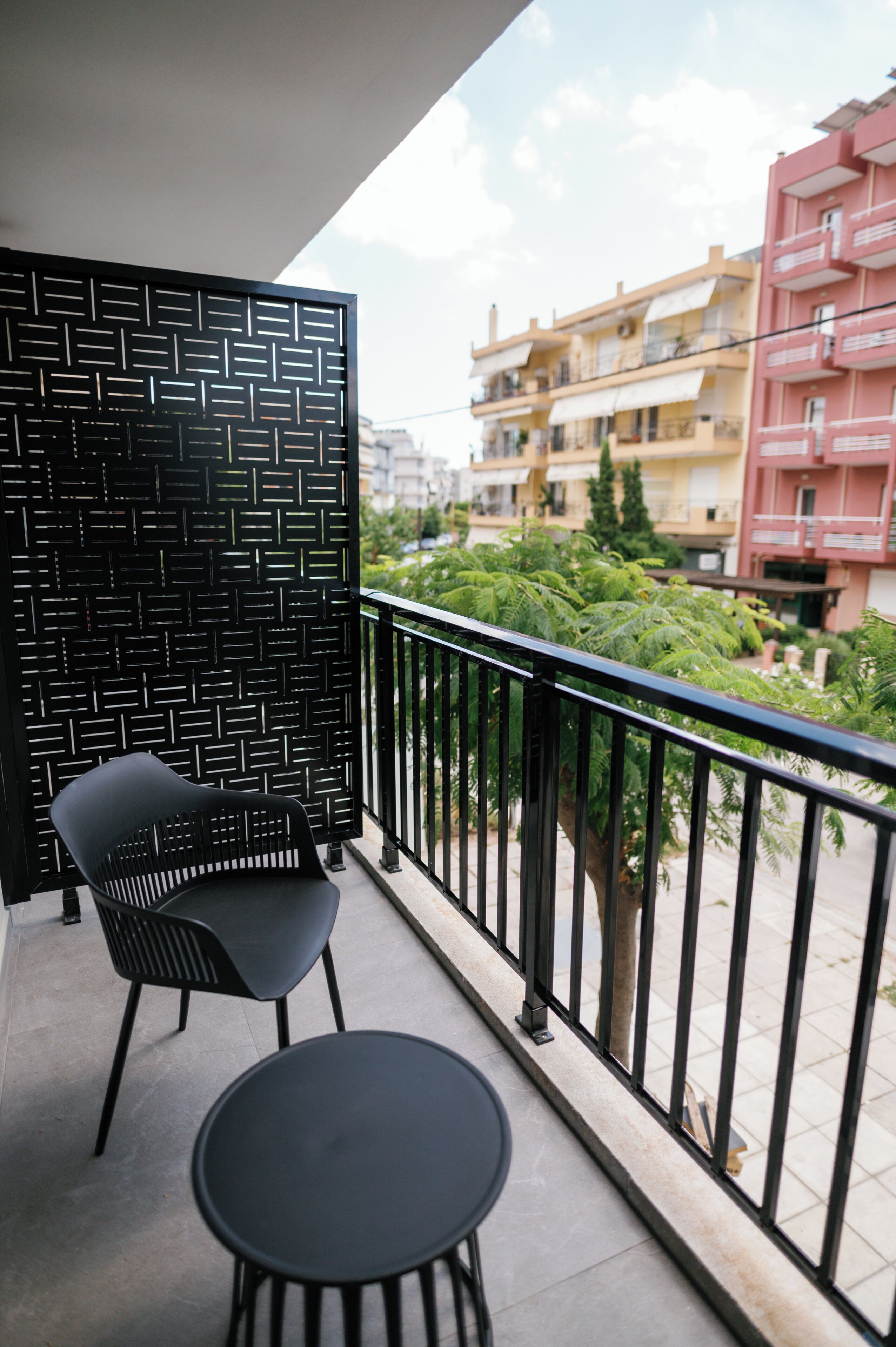 Un balcón con barandilla de metal negro, una silla negra y una pequeña mesa redonda.