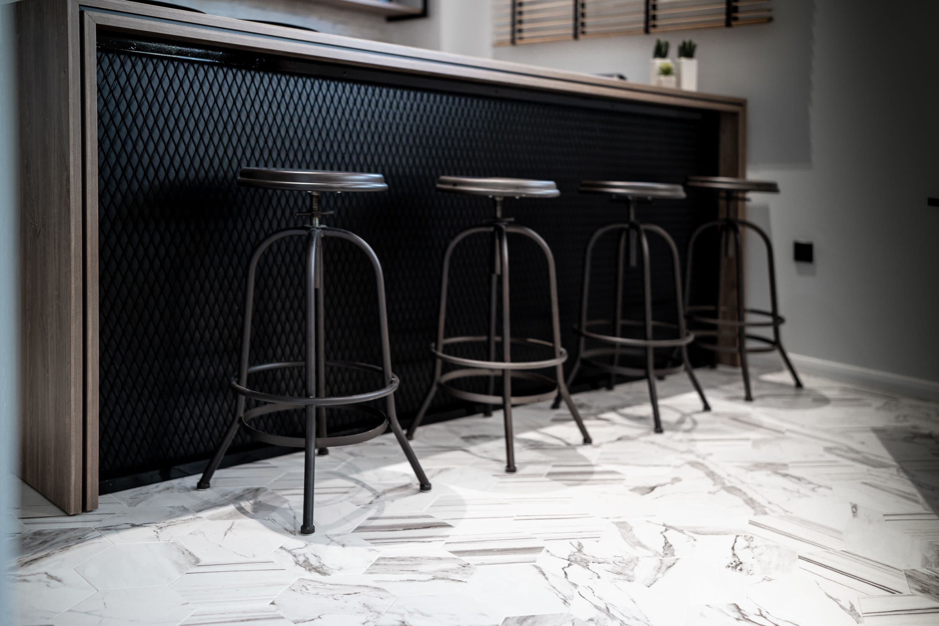 A bar area with four stools, a black textured wall, and a patterned floor.