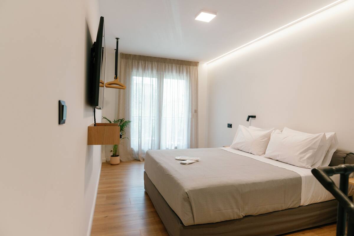 Une chambre moderne avec un grand lit, un téléviseur à écran plat fixé au mur, une plante en pot et un plancher en bois.