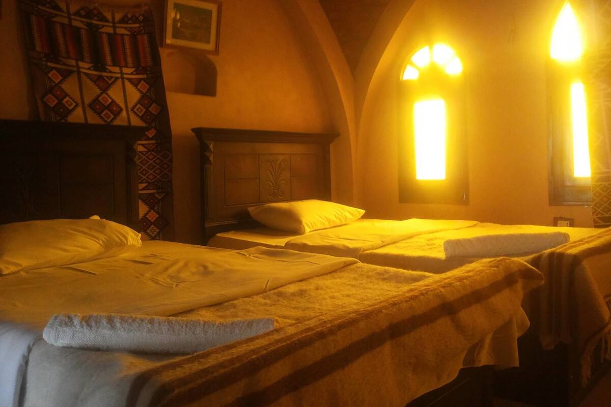 Ein Zimmer mit drei nebeneinanderstehenden Betten, einem Kamin und einem gerahmten Bild an der Wand.
