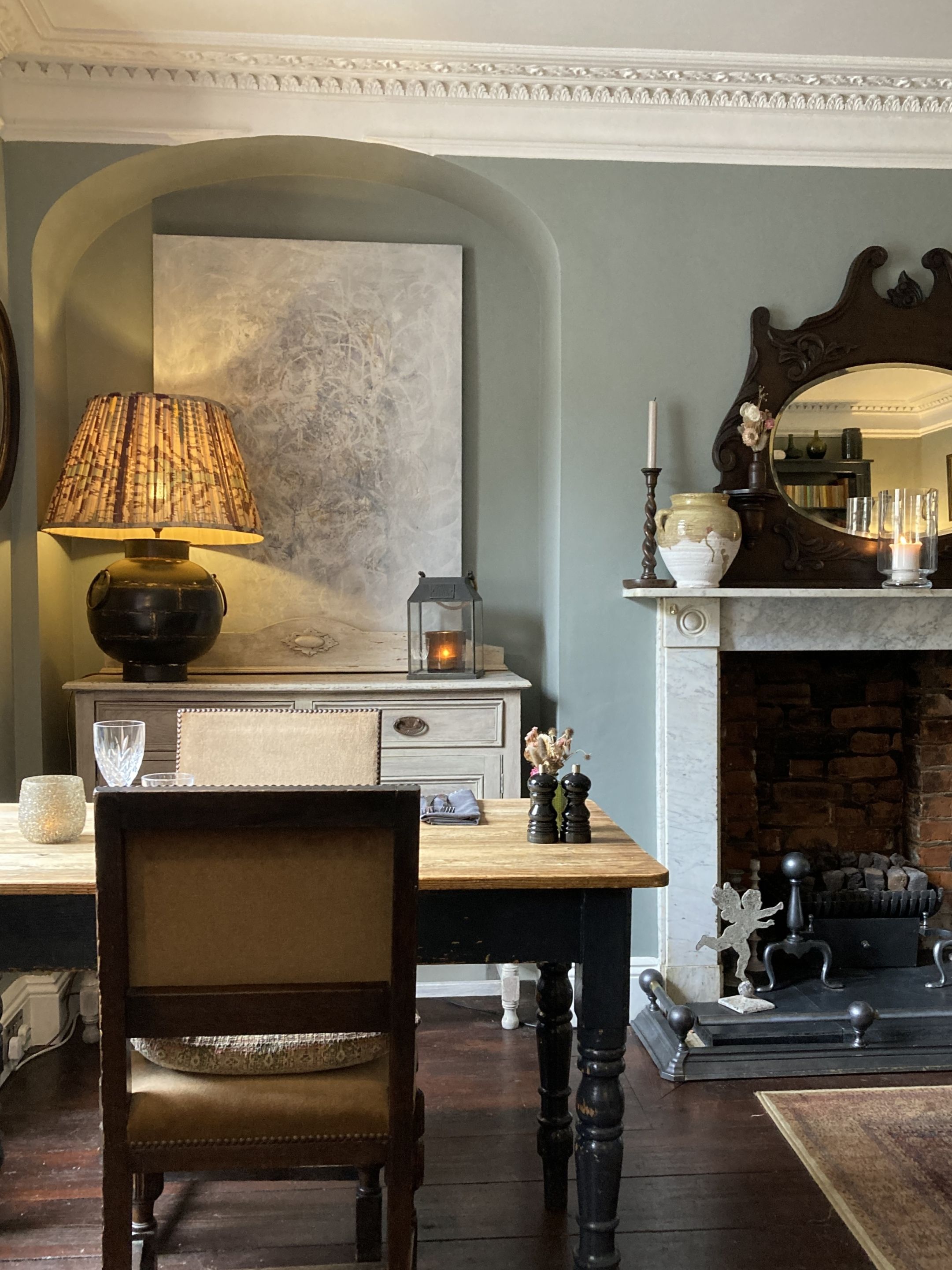 Une pièce avec un bureau en bois, une chaise, une lampe, une cheminée et un grand miroir.