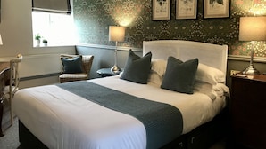 Un dormitorio ordenado con una cama grande, una mesita de noche, una silla y una ventana.