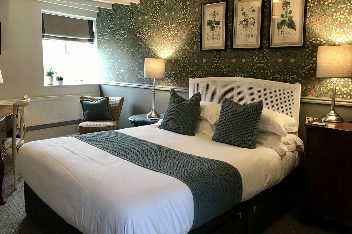 A neatly arranged bedroom with a large bed, a bedside table, a chair, and a window.
