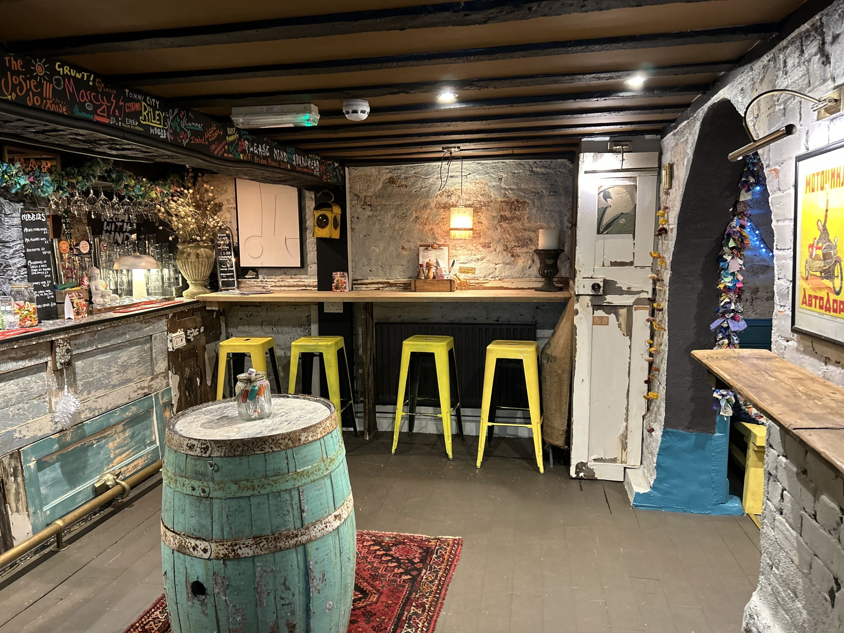 Un coin bar au style rustique, avec un comptoir en bois, des tabourets jaunes et un vieux tonneau.