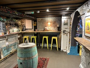 A rustic bar area with a wooden counter, yellow stools, and a vintage barrel.