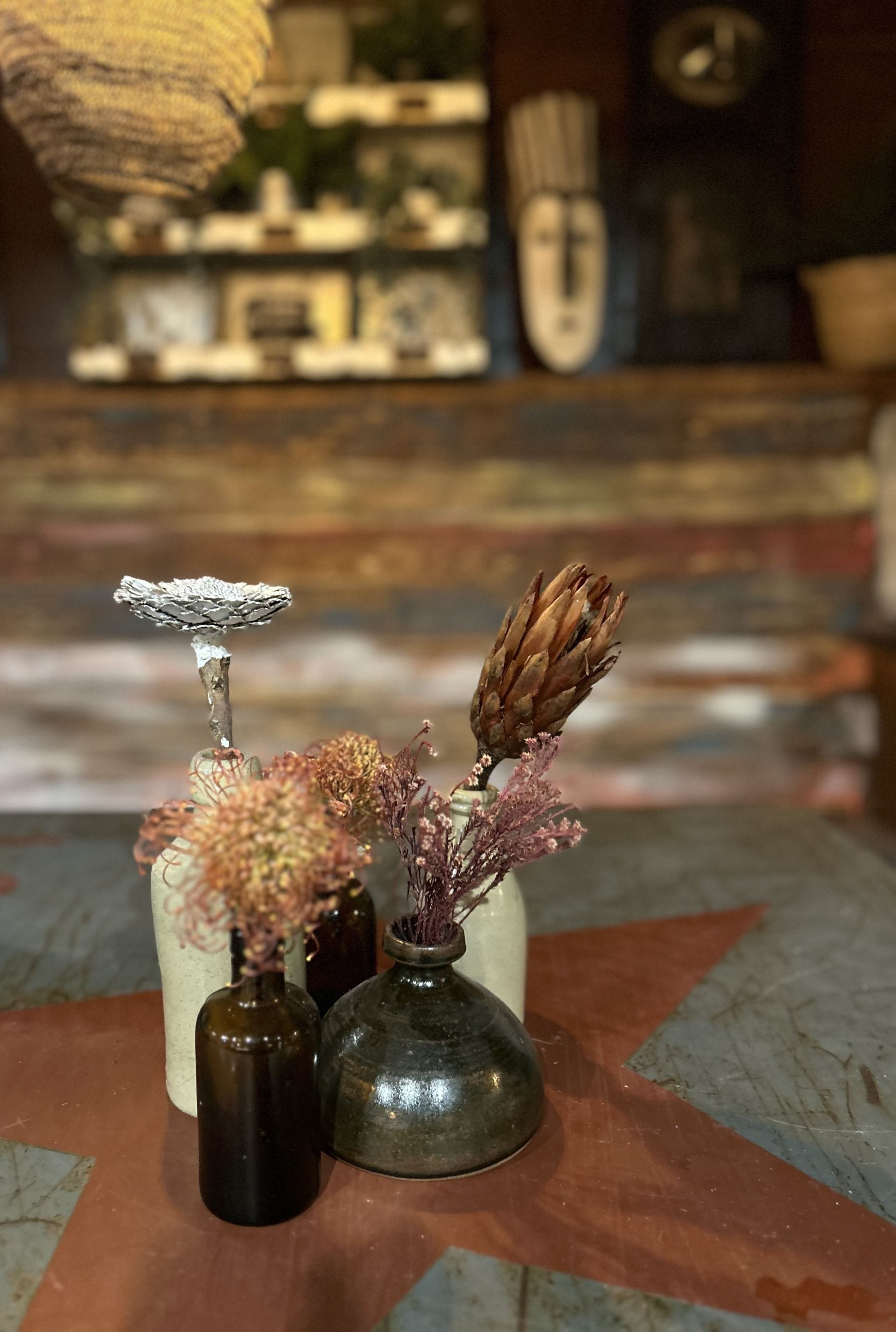 Three small vases with dried plants on a wooden table.