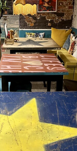 Una habitación con pared de ladrillo rústica, un sofá amarillo, una mesa azul con diseño amarillo y rojo, y un cuadro enmarcado sobre el sofá.