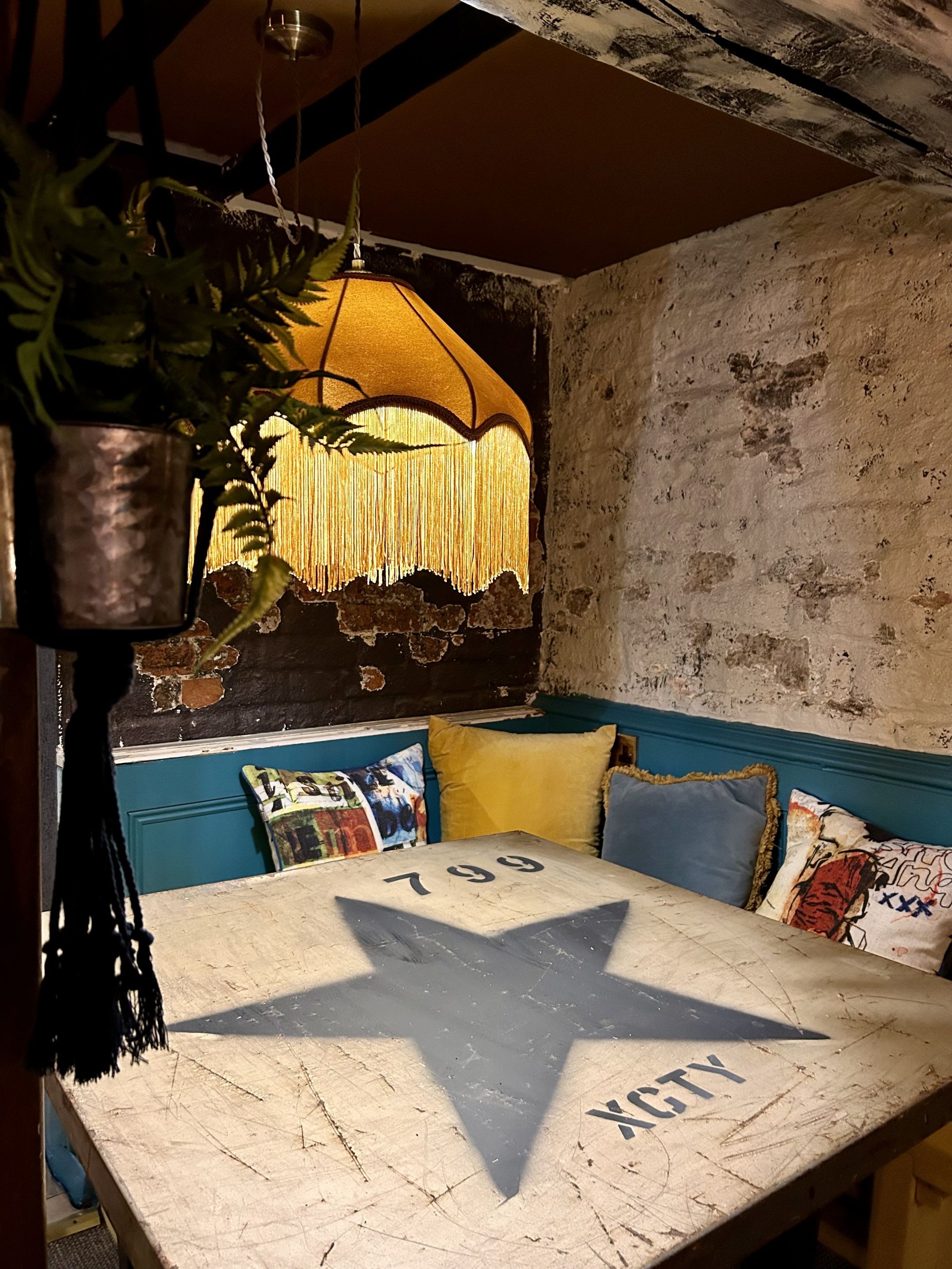 A vintage star-shaped table with the number 799 and the word "AGENCY" on it, set in a rustic room with a distressed wall and a hanging lamp.