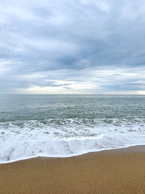 Uma praia com areal e vista para o oceano sob um céu nublado.
