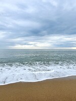 Una playa con arena y vista al océano bajo un cielo nublado.