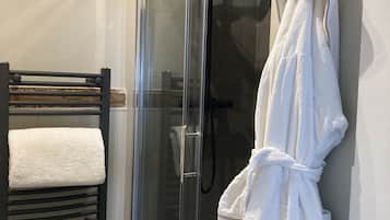 A glass-enclosed shower with a handheld showerhead, a towel rack with a white towel, and a white robe hanging on the wall.