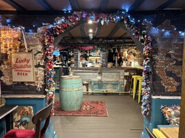 An interior with a rustic brick wall, a bar area with a wooden counter, and a sign reading "Lucky Buddha Enlightened Beer".