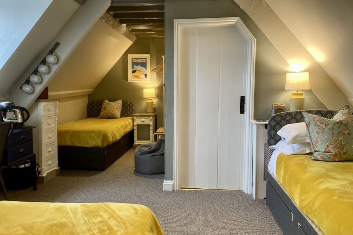 A room with two beds, a white door, and a small desk with a lamp.
