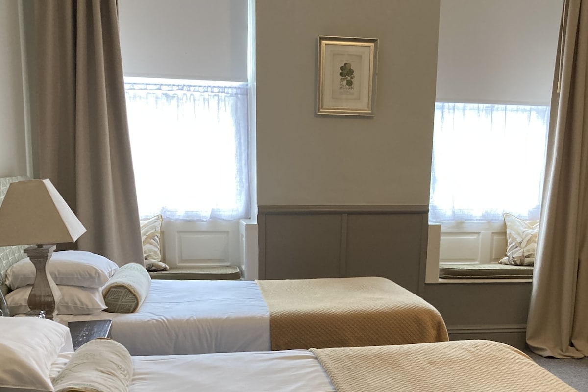 Habitación de hotel con dos camas, una lámpara, un cuadro en la pared y una ventana con cortinas.