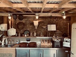 Una cocina rústica con vigas de madera, pared de piedra y diversos utensilios y electrodomésticos de cocina.