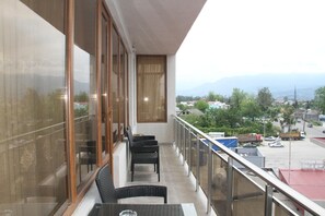 A balcony with wicker furniture, a glass table, and a view of a parking lot and buildings. - Hotel 725 (Batumi)