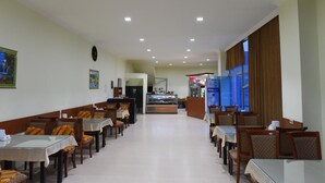 Un restaurant doté de nombreuses tables et chaises, d’un comptoir avec une vitrine, et offrant une vue sur l’extérieur grâce à de grandes fenêtres.