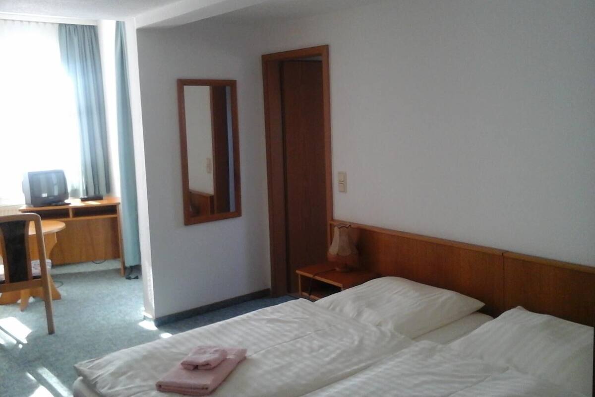 A hotel room with a bed, a desk, a chair, a television, and a mirror.