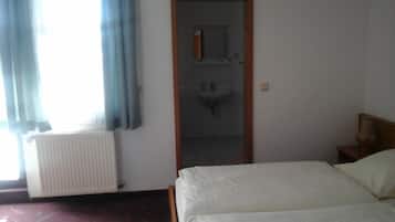 Ein Hotelzimmer mit einem Bett, einem Heizkörper, einem Fenster mit Vorhängen und einer Tür zu einem Badezimmer mit Waschbecken.