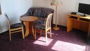 A small room with a sofa, two chairs, a small round table, a lamp, a desk with a computer monitor, and a patterned carpet. - Landhotel zur Krone (Krayenberggemeinde)