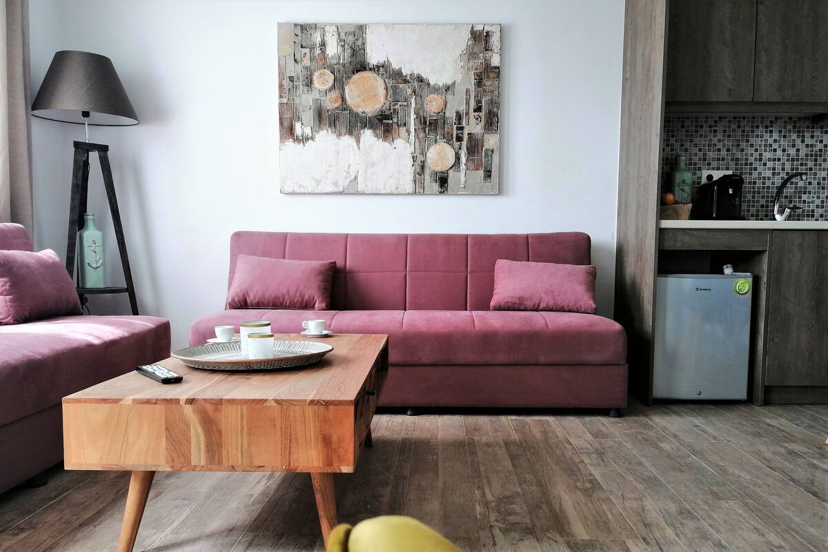 Uma sala de estar moderna com um sofá rosa, uma mesa de centro de madeira e uma pintura abstrata minimalista na parede.