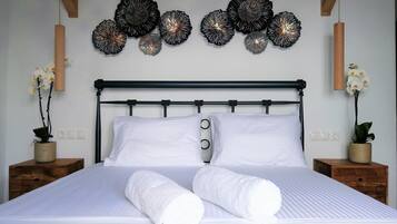 A neatly made bed with white linens and two rolled towels, a black metal headboard, and decorative wall art above.