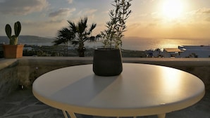 Une table ronde, ornée d’un pot de fleurs au centre, offre une vue imprenable sur la côte, avec le soleil se couchant sur la mer.