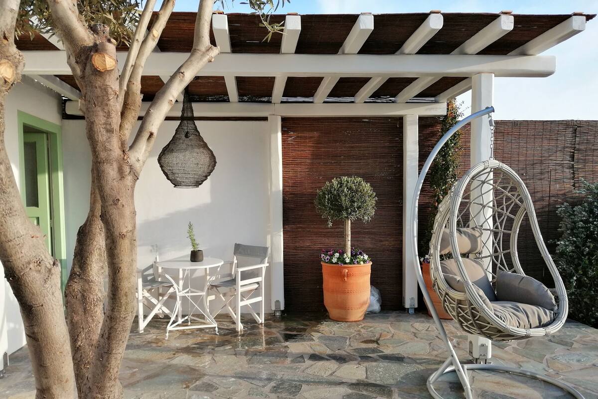 Uma área de pátio com uma cadeira suspensa, uma mesa pequena com cadeiras e um vaso com planta.