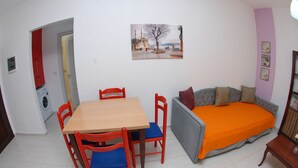 A compact living space with a dining table, chairs, a sofa, and a bed. - Wave Apartments Sarande (Sarandë)