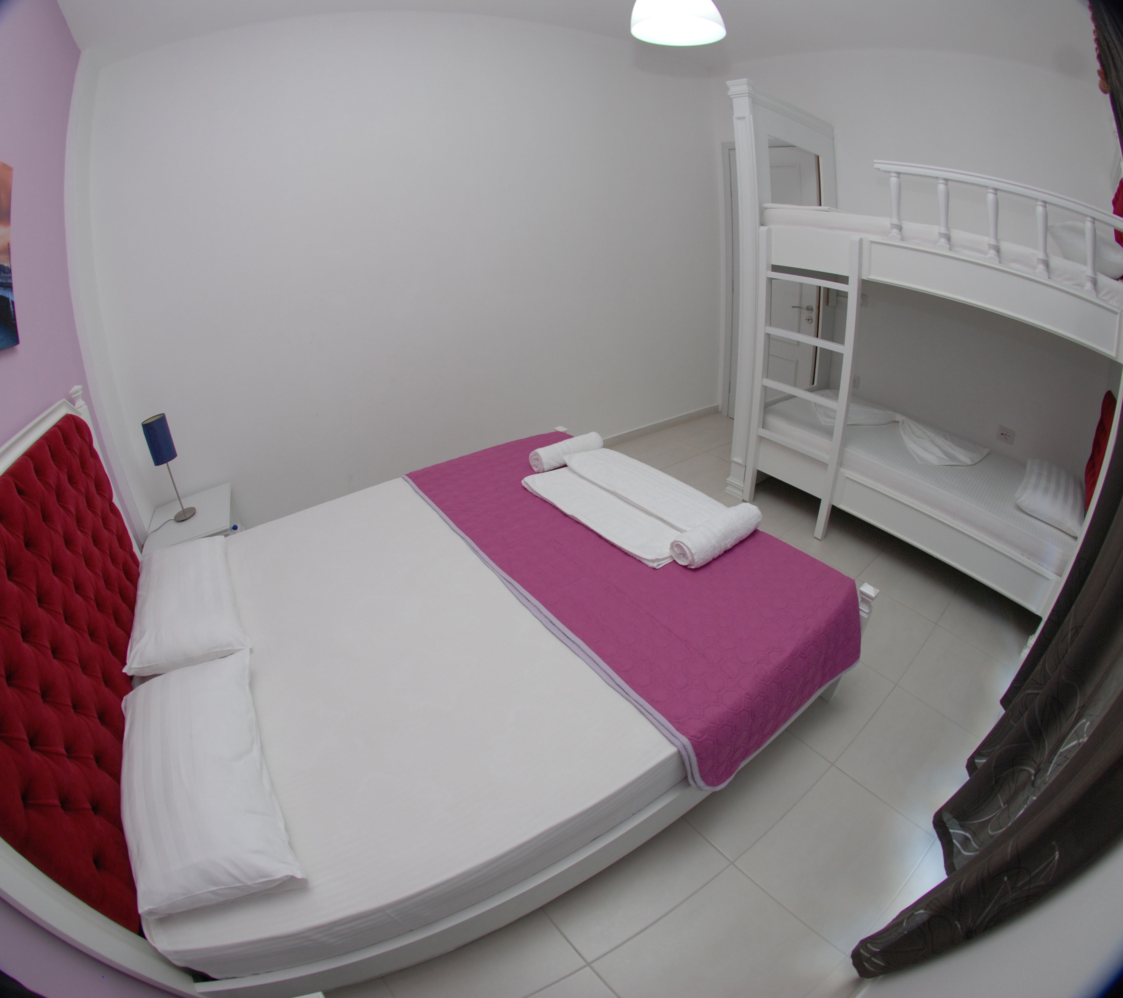 Ein Zimmer mit einem Etagenbett, einem Einzelbett mit rotem Kopfteil und einem kleinen Nachttisch mit Lampe.