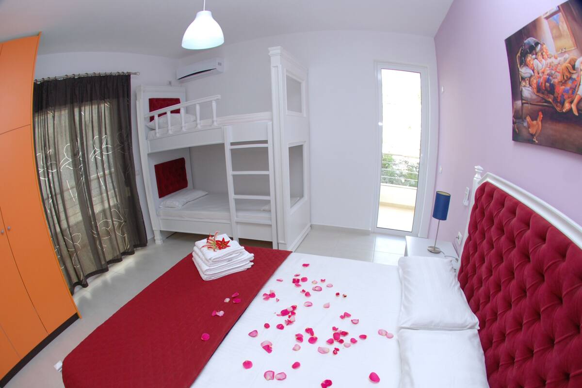 A hotel room with a large bed, a bunk bed, a red and white color scheme, and a painting on the wall.