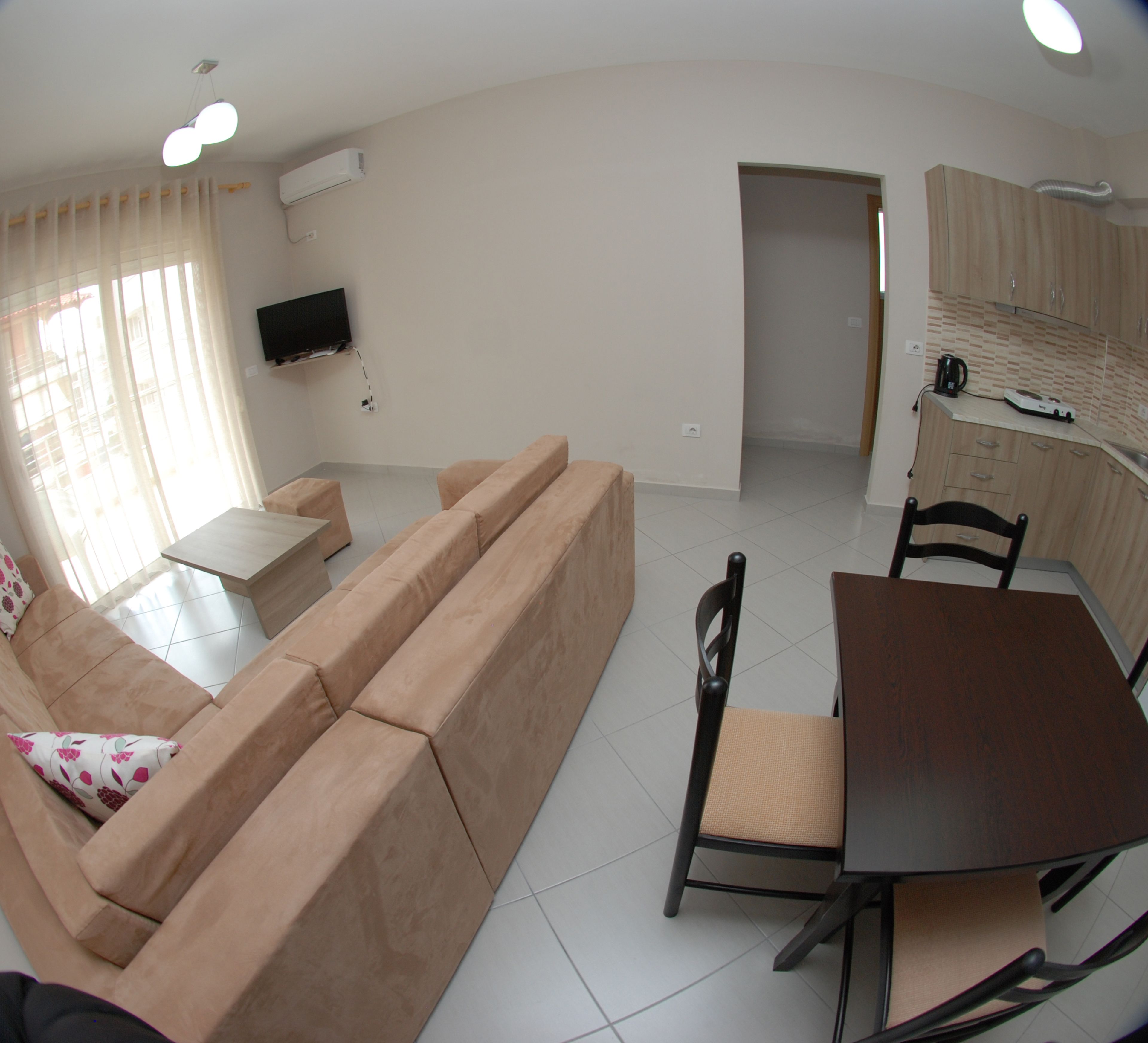 A living room with a beige sofa, a small table, and a TV mounted on the wall.
